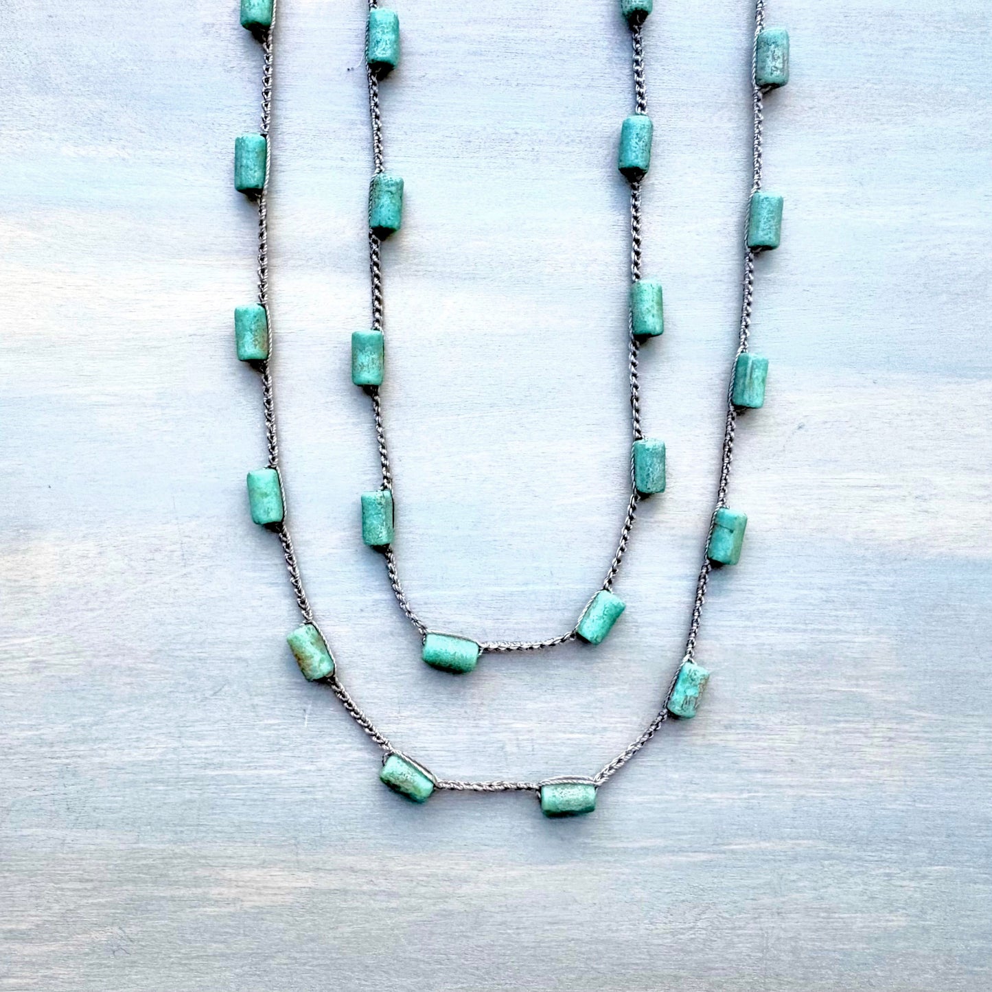 Two turquoise beaded necklaces on a light wooden surface