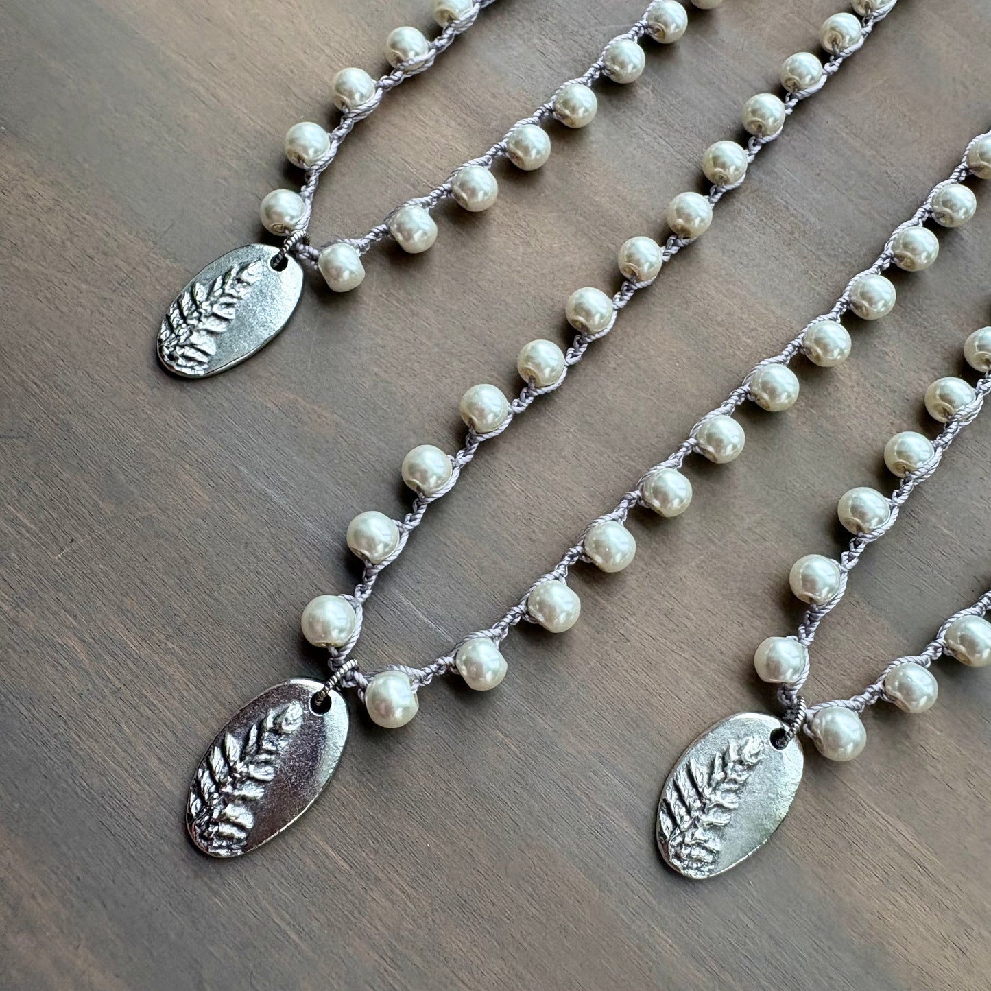 Two pearl necklaces with silver leaf pendants on a wooden surface