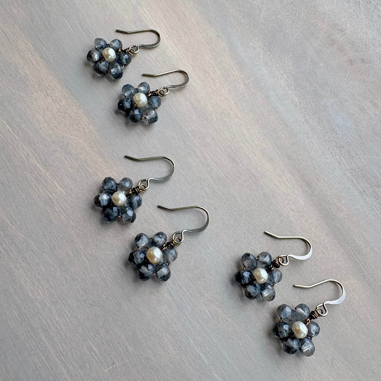 Set of flower-shaped earrings with blue and pearl beads on a wooden surface