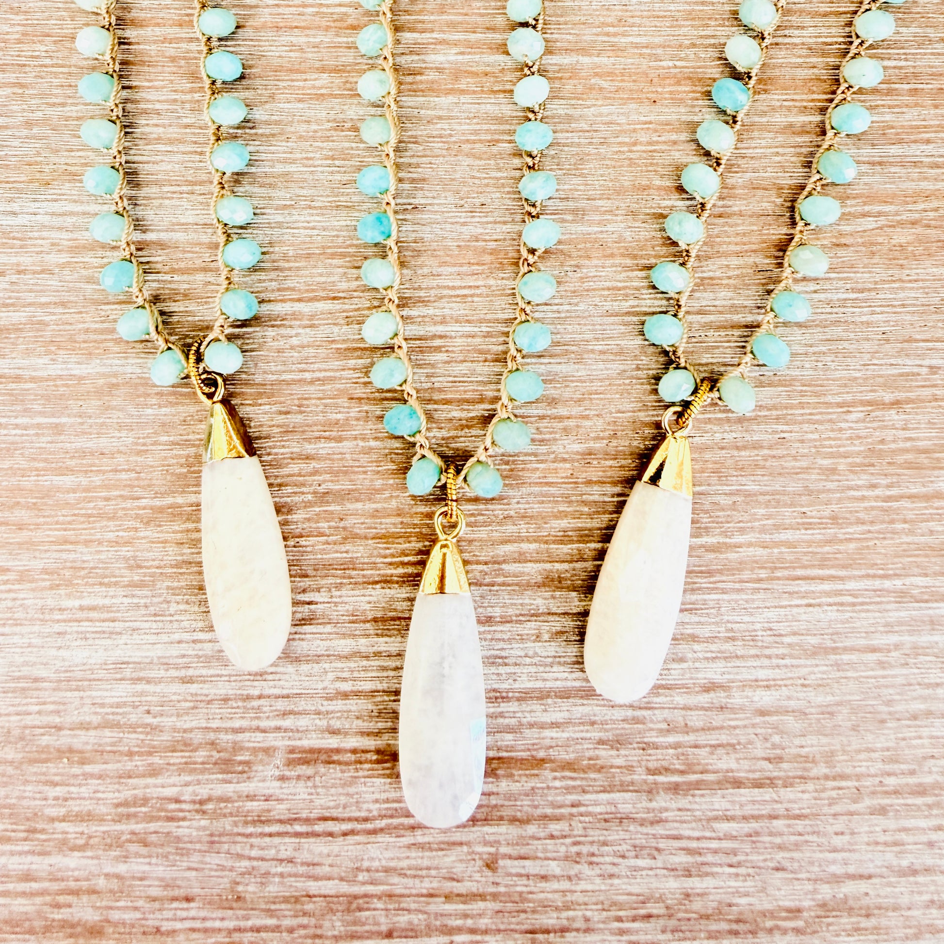 Three necklaces with light blue beads and white teardrop pendants on a wooden surface