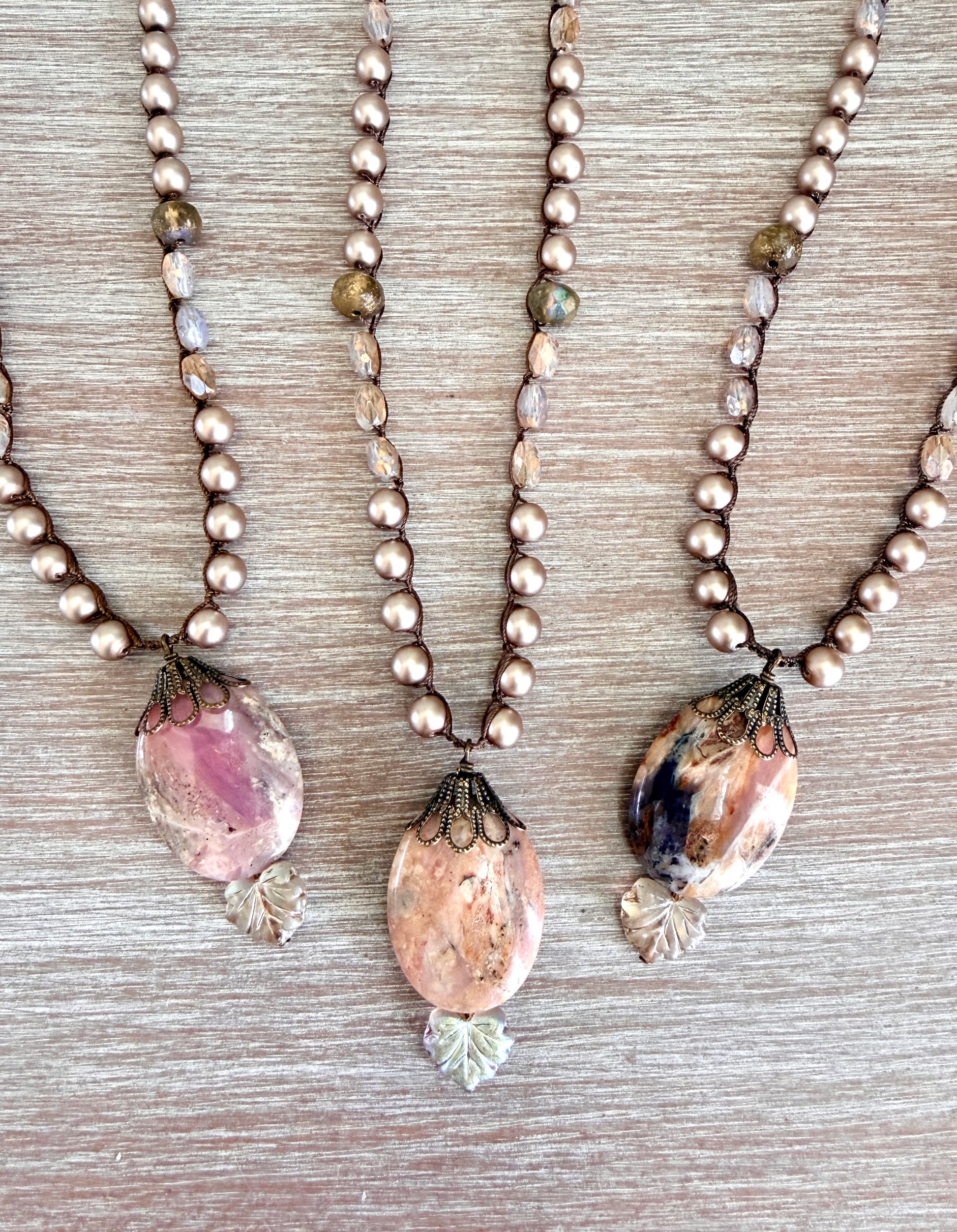 Three pearl necklaces with stone pendants on a wooden surface