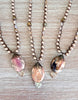Three pearl necklaces with stone pendants on a wooden surface