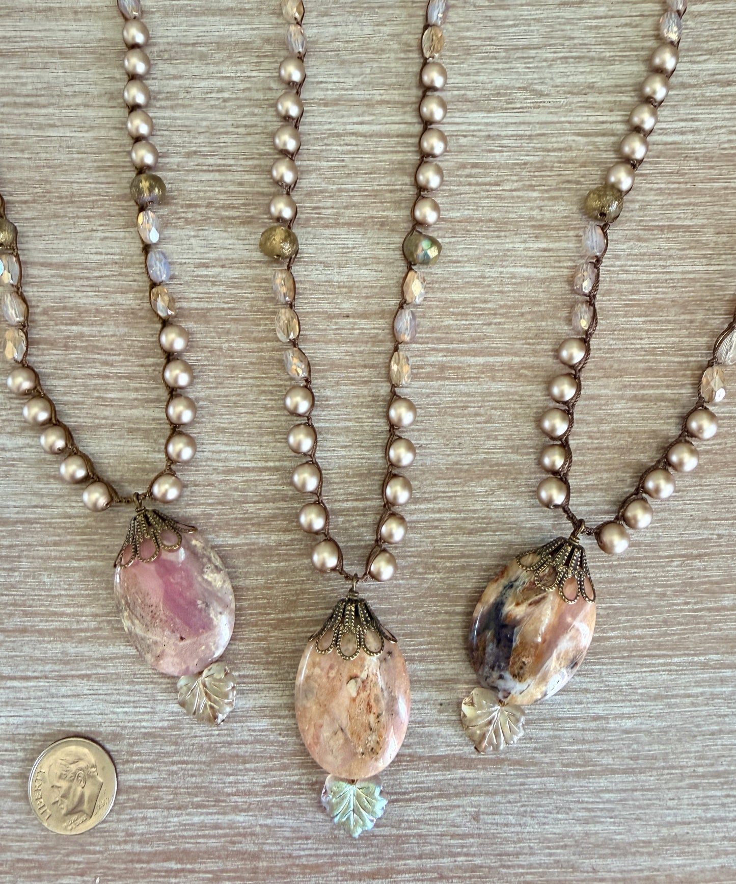Three pearl necklaces with pendant stones on a wooden surface, one with a coin for scale.