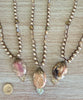 Three pearl necklaces with pendant stones on a wooden surface, one with a coin for scale.