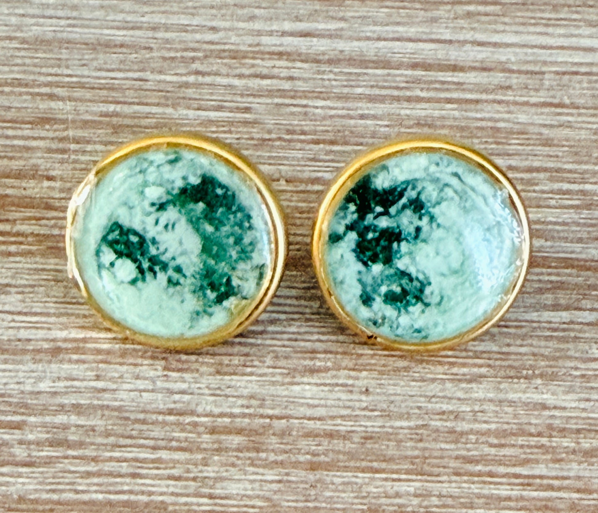 Pair of earrings with greenstone stones in gold settings on a wooden surface