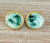 Pair of earrings with greenstone stones in gold settings on a wooden surface