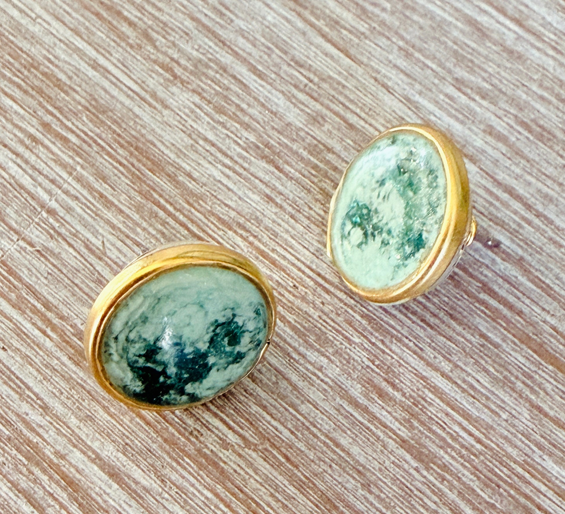 Pair of earrings with green stone and gold setting on a wooden surface