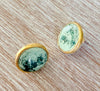 Pair of earrings with green stone and gold setting on a wooden surface