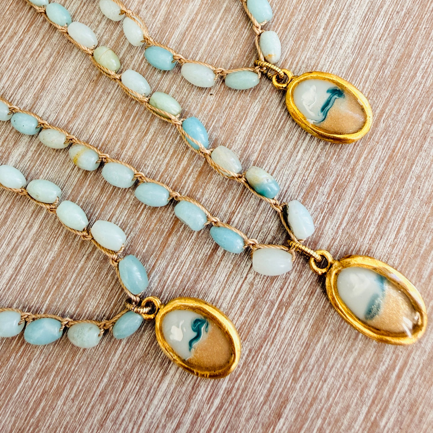 Two gold necklaces with blue beads and oval pendants on a wooden surface