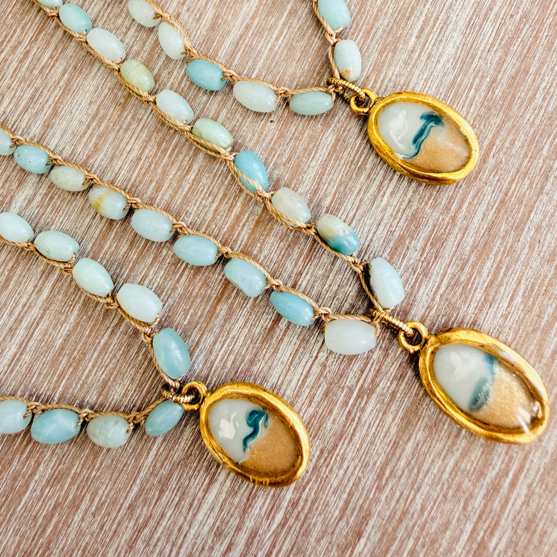 Two gold necklaces with blue beads and oval pendants on a wooden surface