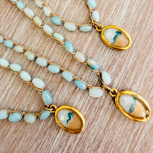 Two gold necklaces with blue beads and oval pendants on a wooden surface