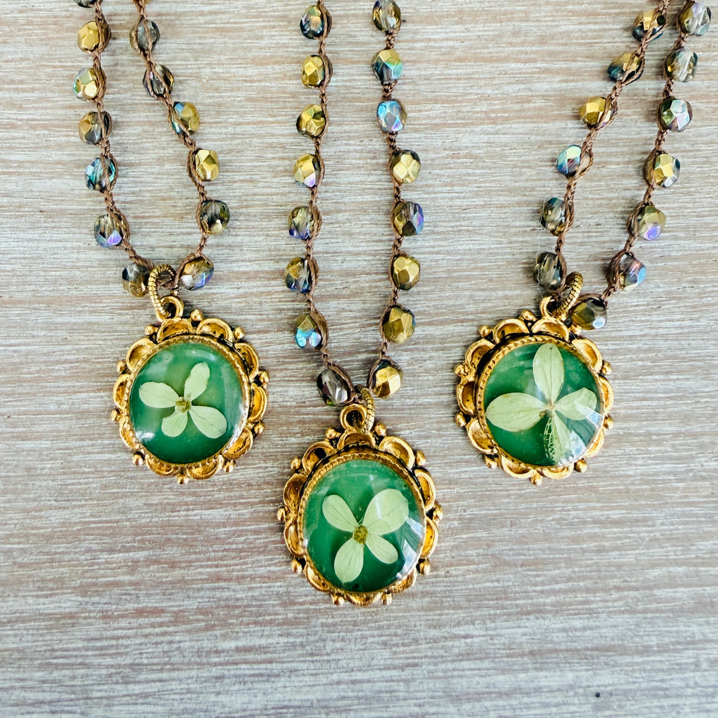 Three necklaces with green floral pendants on a textured surface