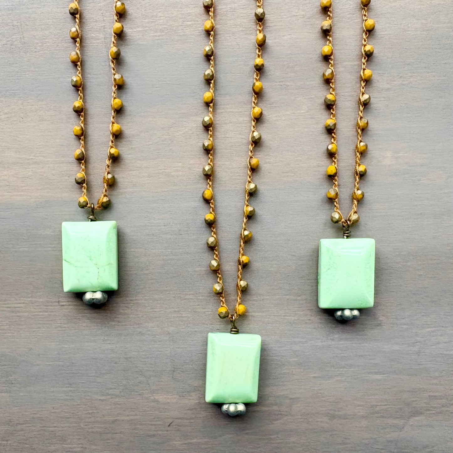 Three necklaces with green pendants on a wooden surface