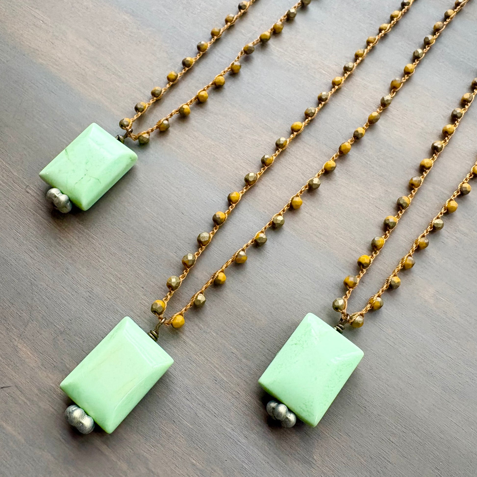 Three necklaces with green stone square pendants and gold crocheted beads on a wooden surface.