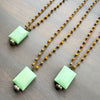 Three necklaces with green stone square pendants and gold crocheted beads on a wooden surface.