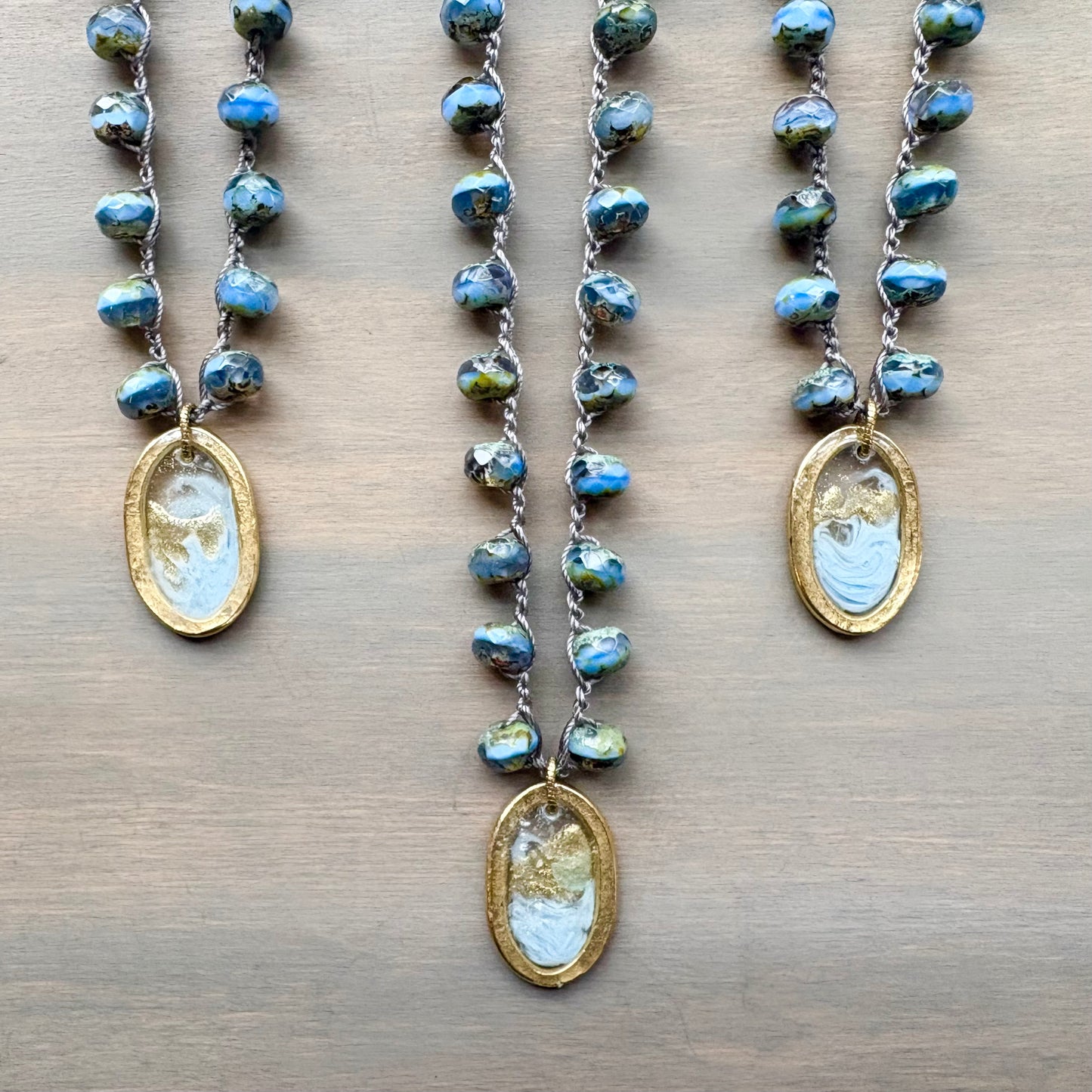Three necklaces with blue beaded chains and gold pendants on a wooden surface