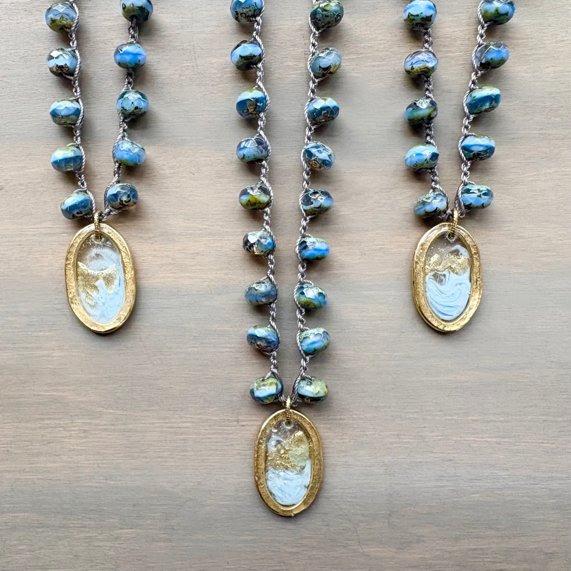 Three necklaces with blue beaded chains and gold pendants on a wooden surface