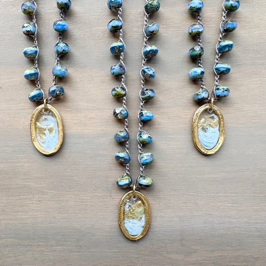 Three necklaces with blue beaded chains and gold pendants on a wooden surface
