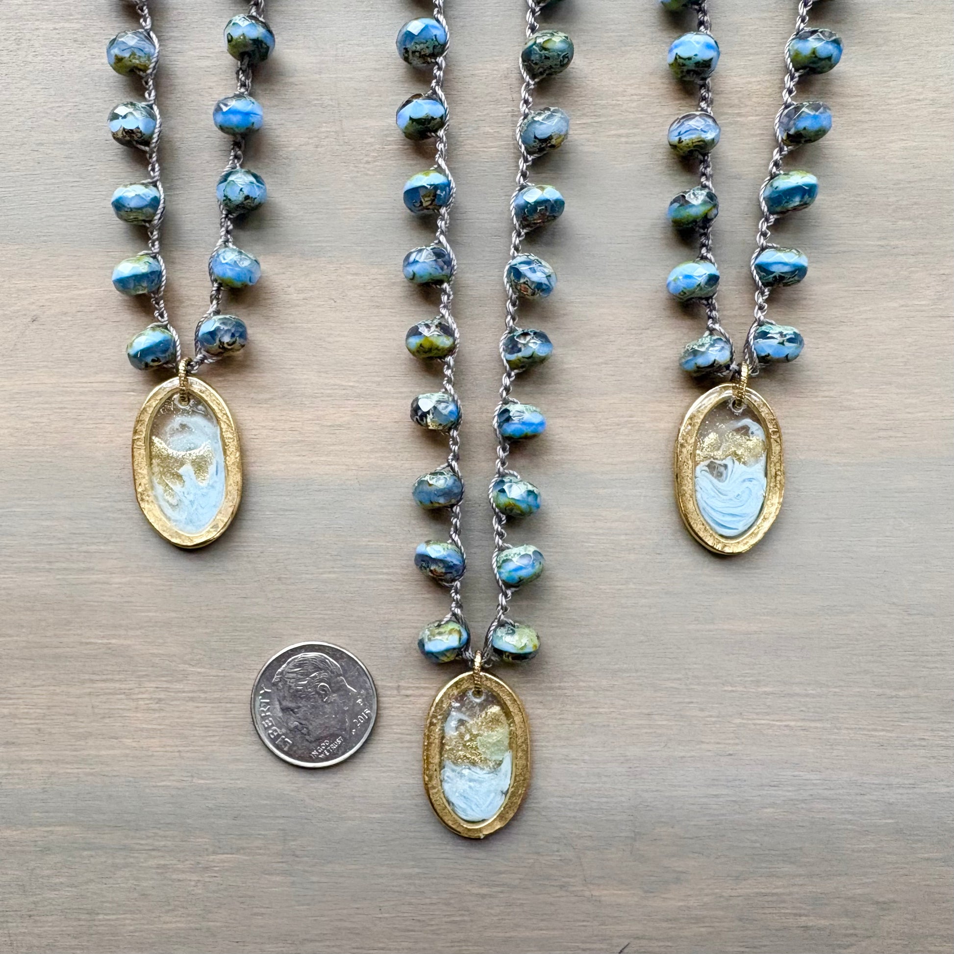 Three necklaces with pendant stones on a wooden surface, one with a coin for scale.