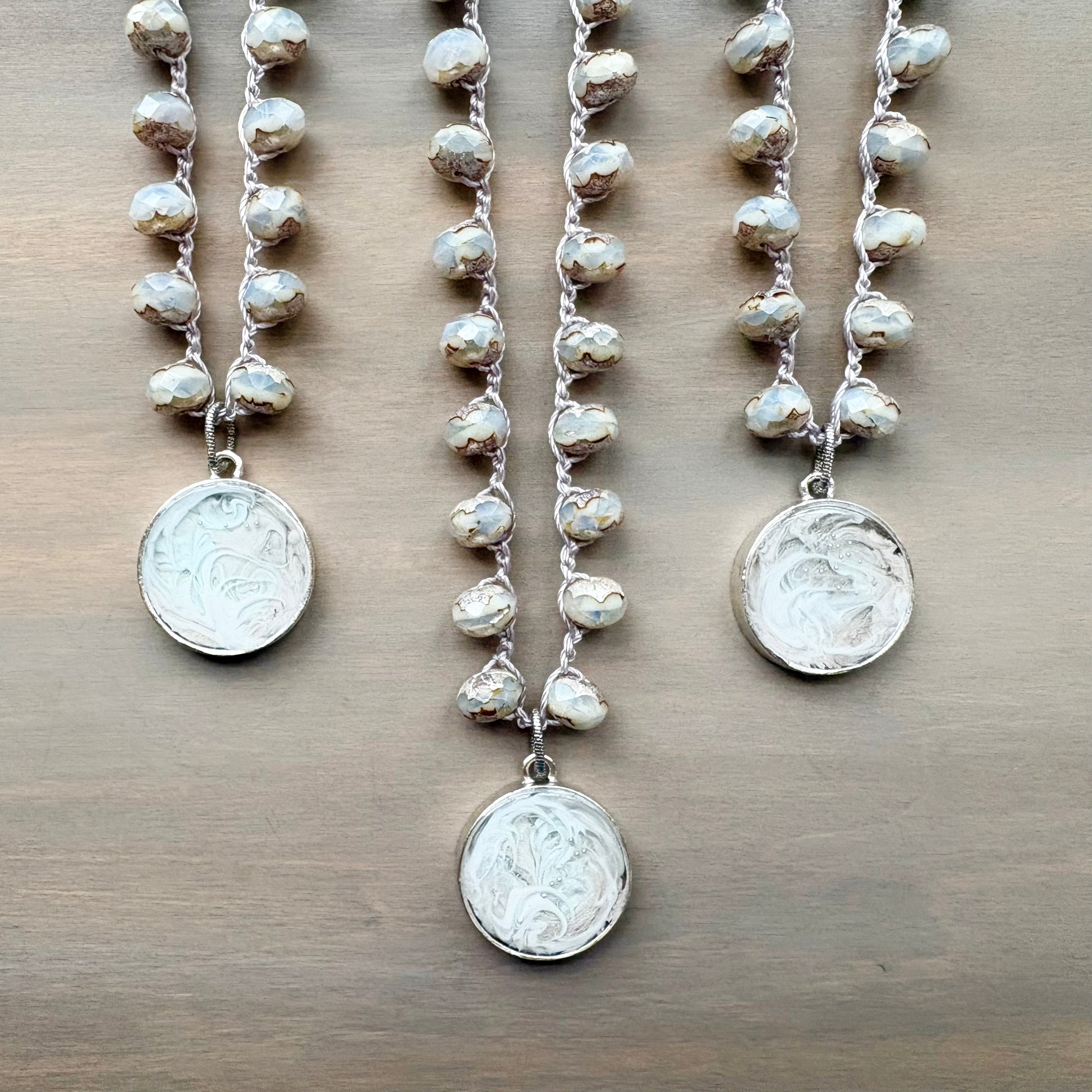 Three crocheted crystal pearl necklaces with snowy coin pendants on a wooden surface