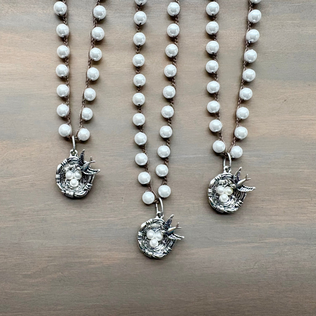 Three pearl necklaces with silver bird nest pendants on a wooden surface