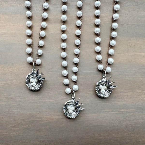 Three pearl necklaces with silver bird nest pendants on a wooden surface