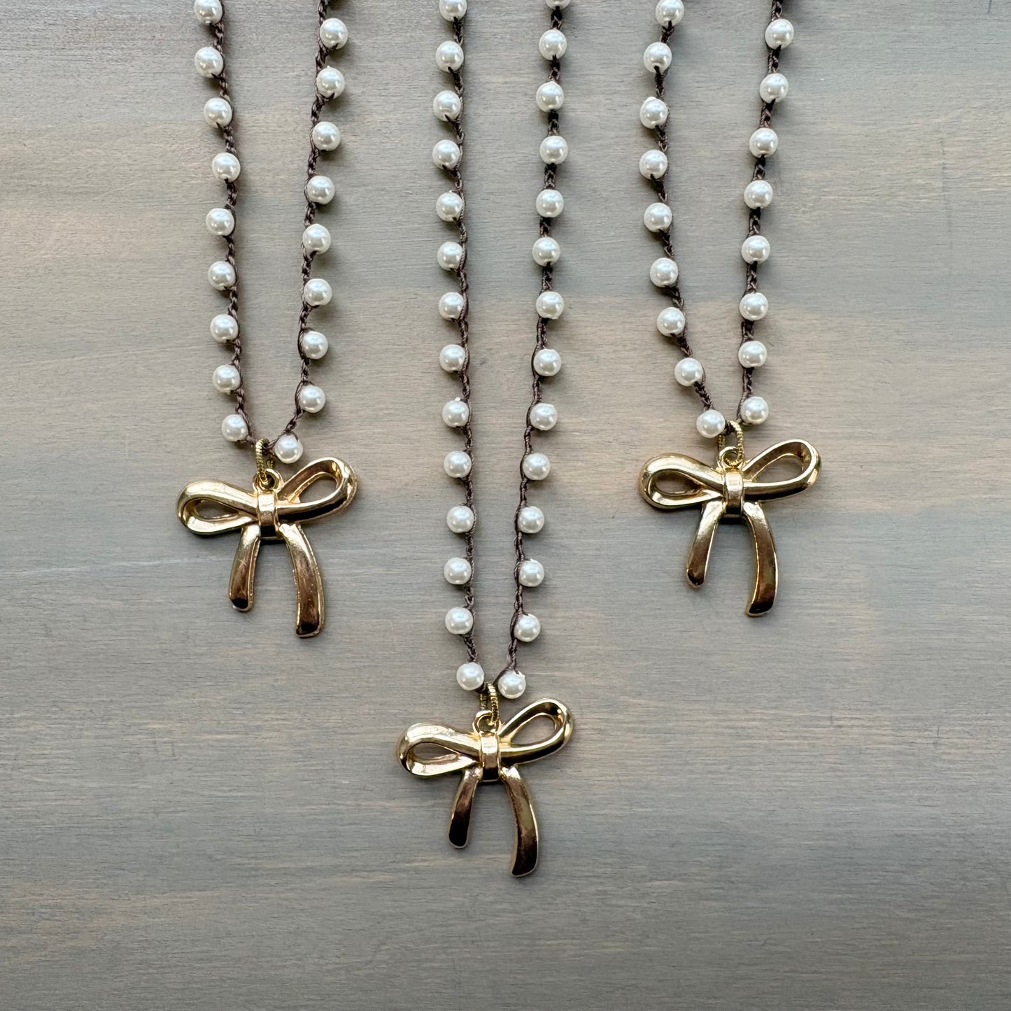 Three pearl necklaces with gold bow pendants on a wooden surface