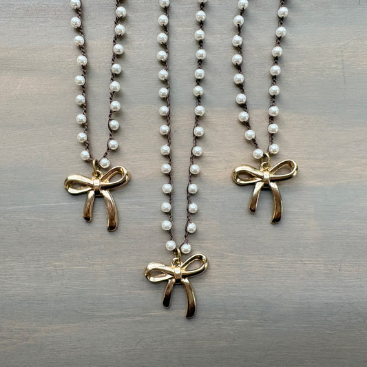 Three pearl necklaces with gold bow pendants on a wooden surface