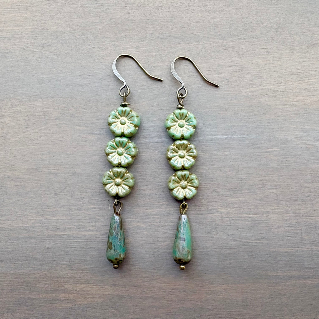 Pair of green floral earrings on a metallic surface