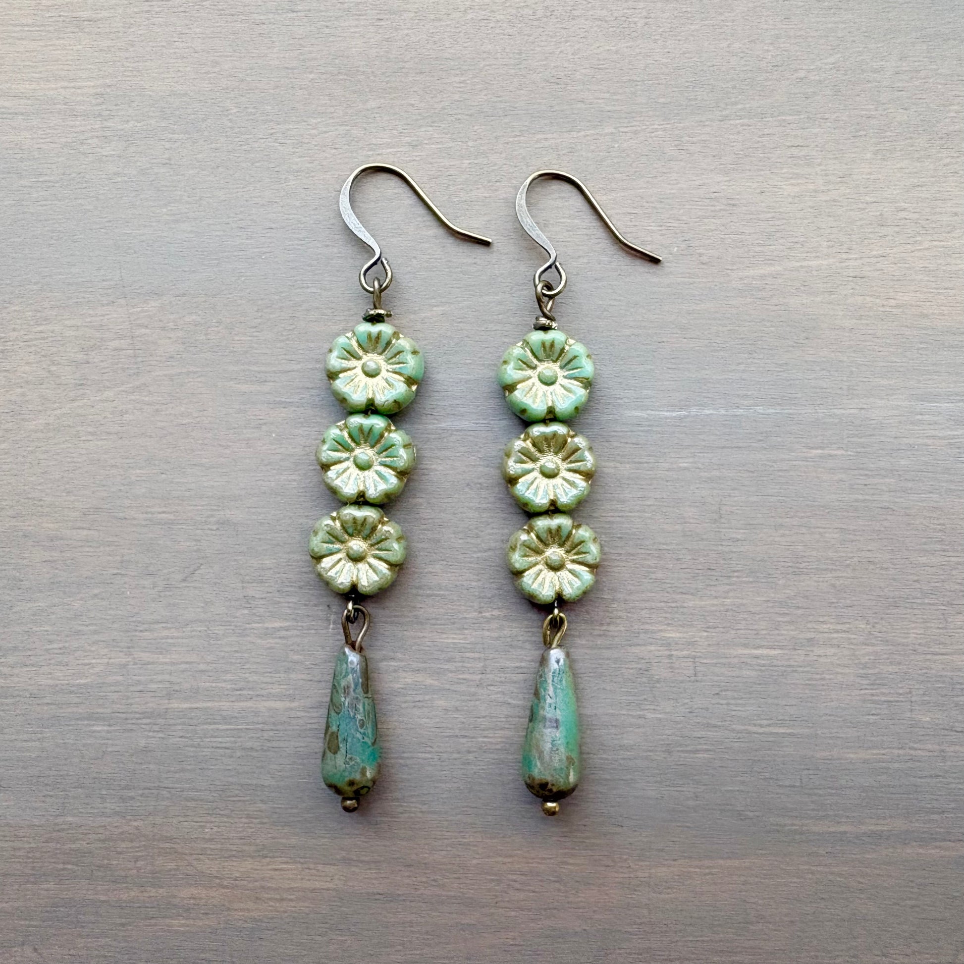 Pair of green floral earrings on a metallic surface