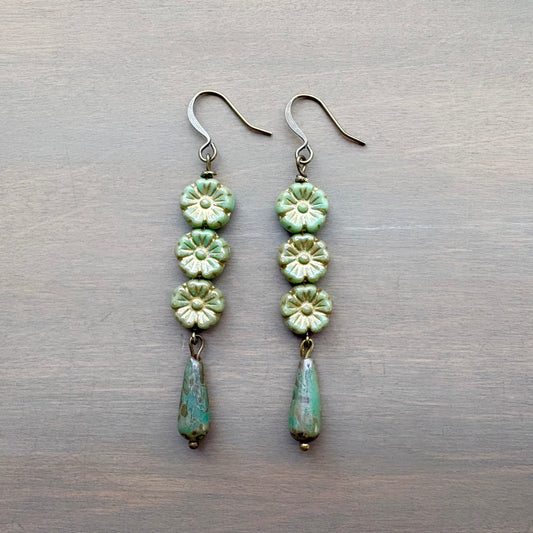 Pair of green floral earrings on a metallic surface