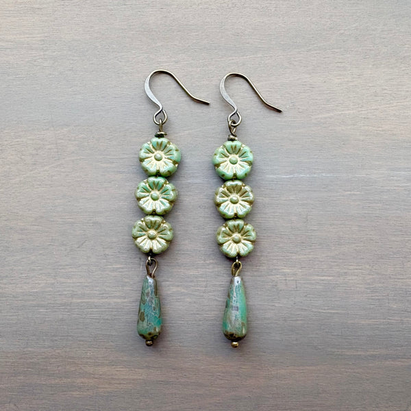 Pair of green floral earrings on a metallic surface