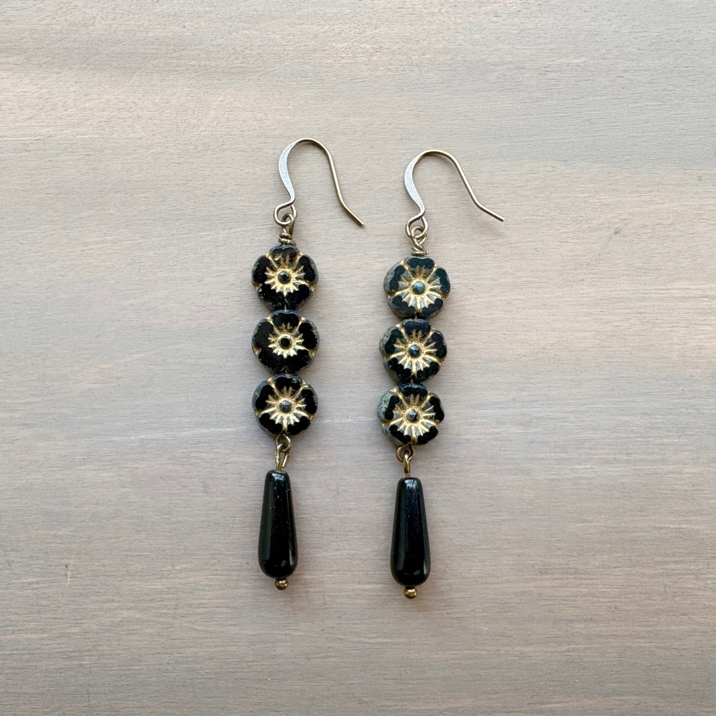 Pair of earrings with black and gold flower beads on a metallic surface