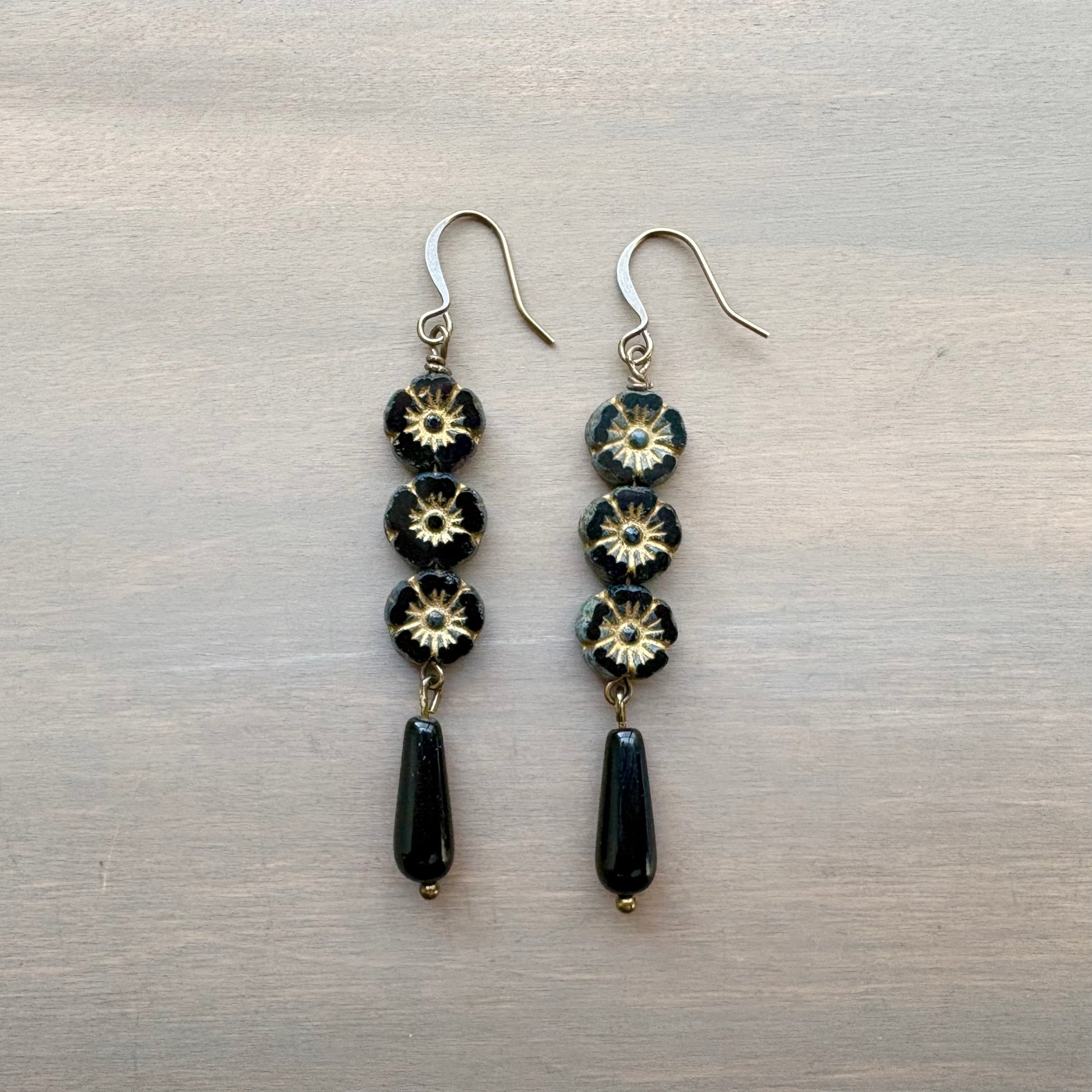 Pair of earrings with black and gold flower beads on a metallic surface