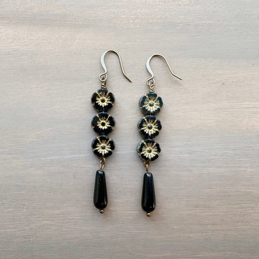 Pair of earrings with black and gold flower beads on a metallic surface
