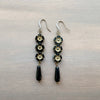 Pair of earrings with black and gold flower beads on a metallic surface