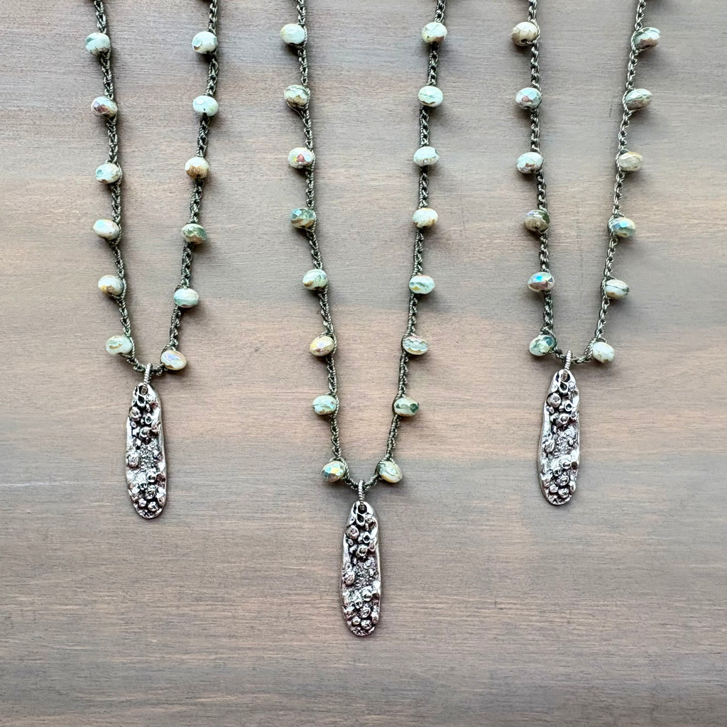 Three pearl necklaces with silver pendants on a wooden surface