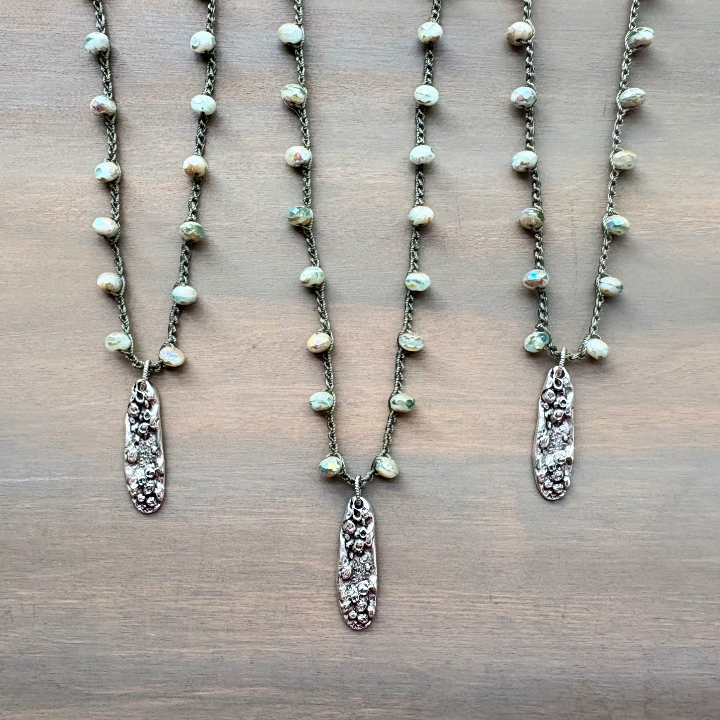 Three pearl necklaces with silver pendants on a wooden surface