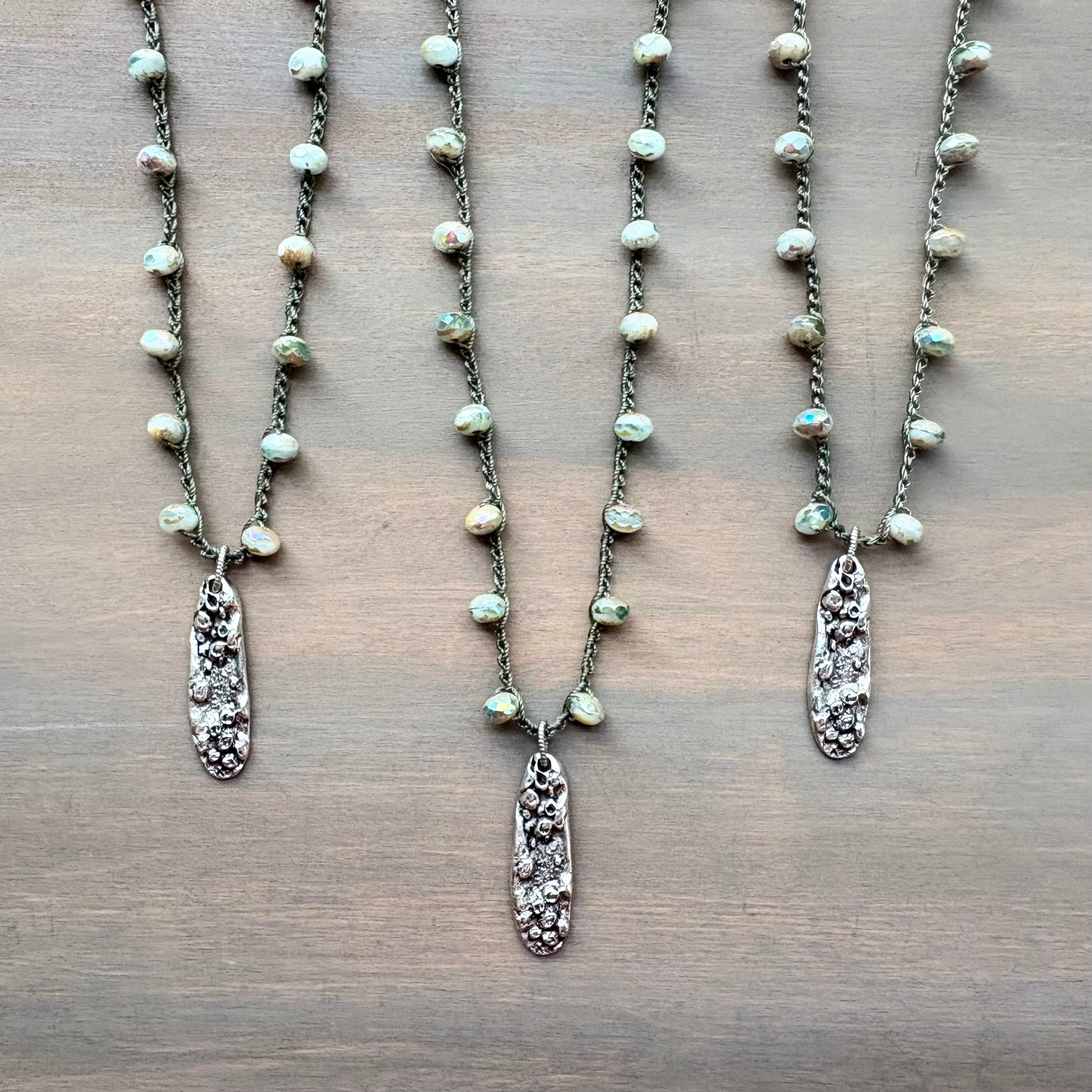 Three pearl necklaces with silver pendants on a wooden surface