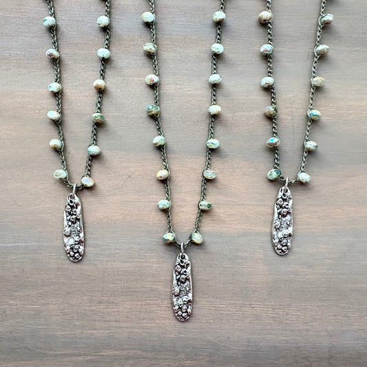 Three pearl necklaces with silver pendants on a wooden surface