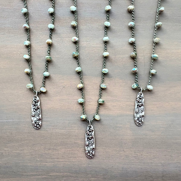 Three pearl necklaces with silver pendants on a wooden surface