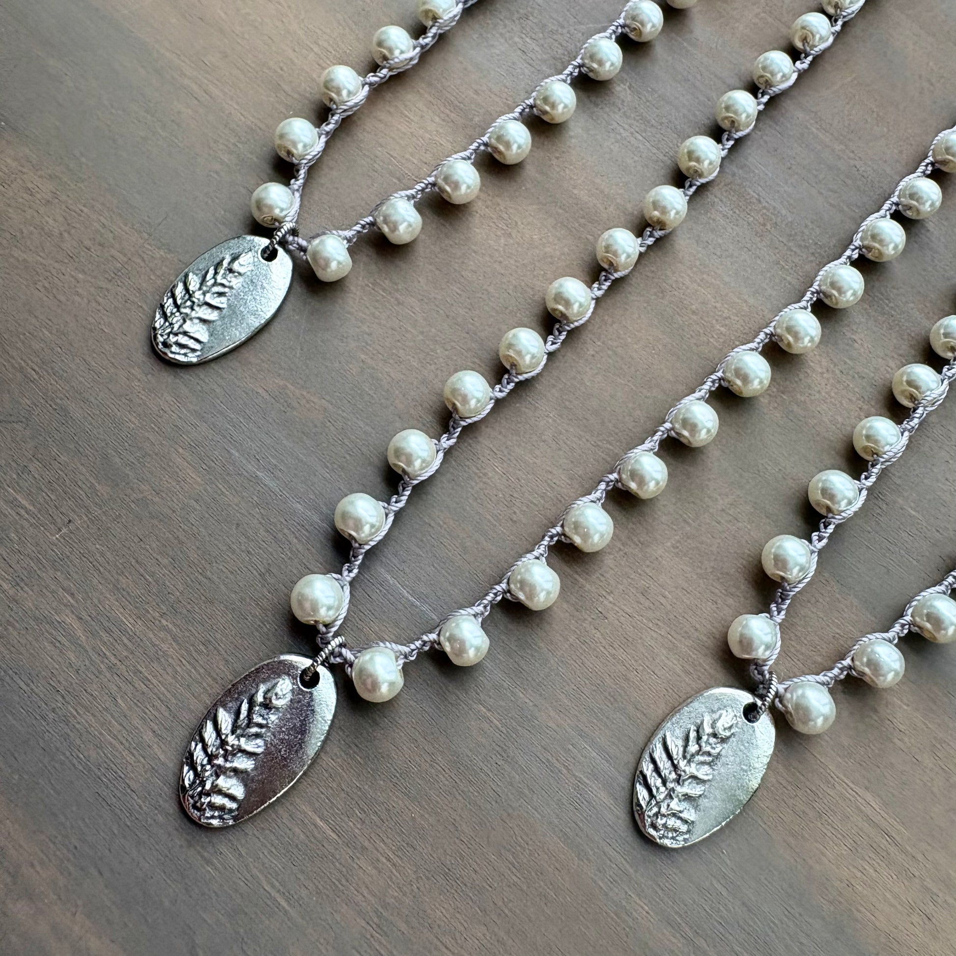 Two pearl necklaces with silver leaf pendants on a wooden surface