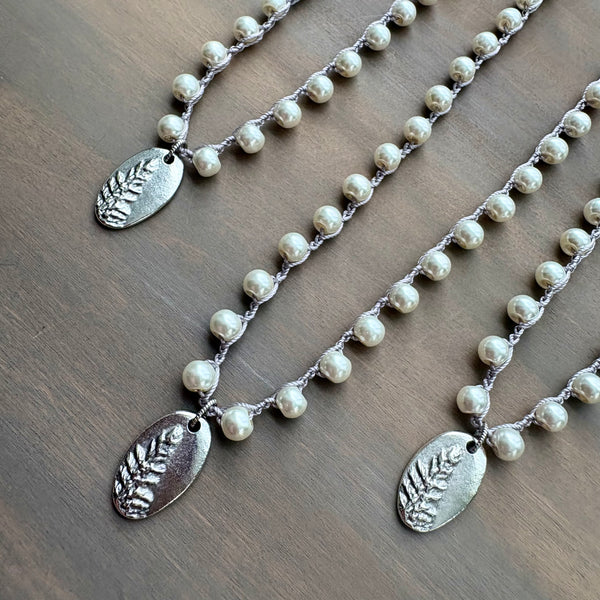 Two pearl necklaces with silver leaf pendants on a wooden surface