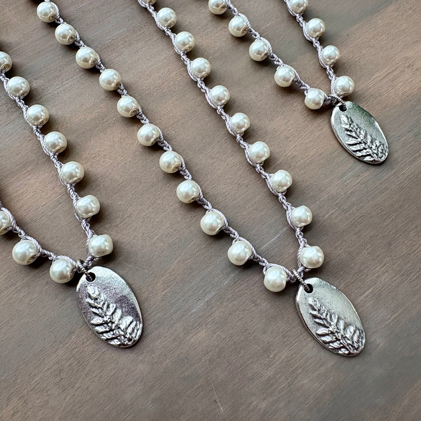 Three pearl necklaces with silver leaf pendants on a wooden surface