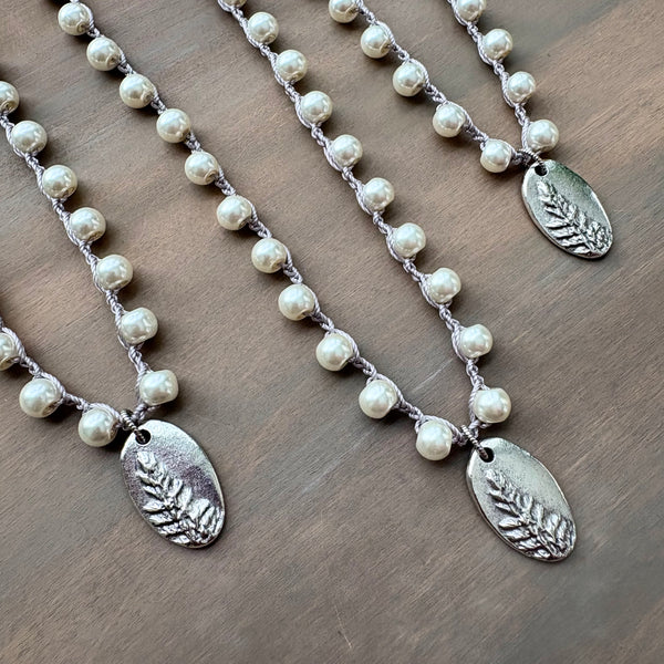 Three pearl necklaces with silver leaf pendants on a wooden surface