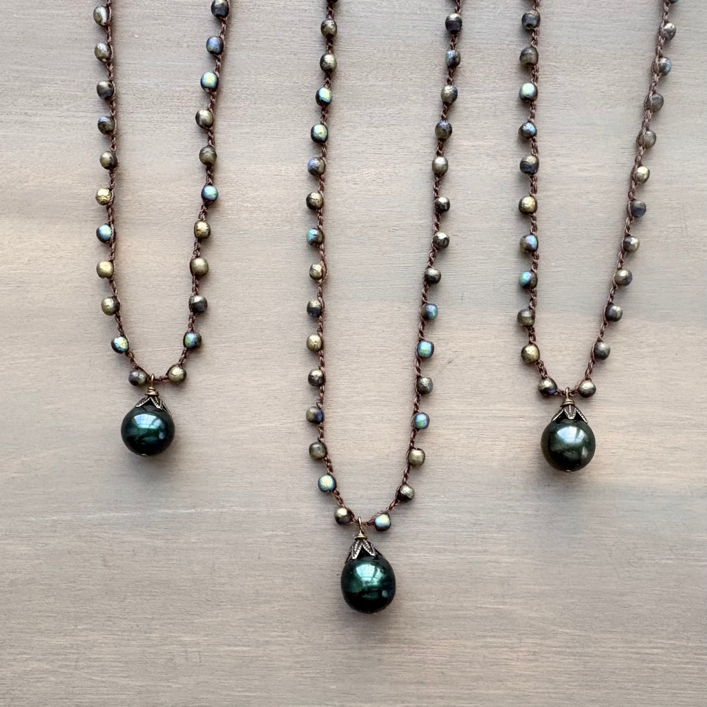 Three pearl necklaces with green teardrop pendants on a beige surface
