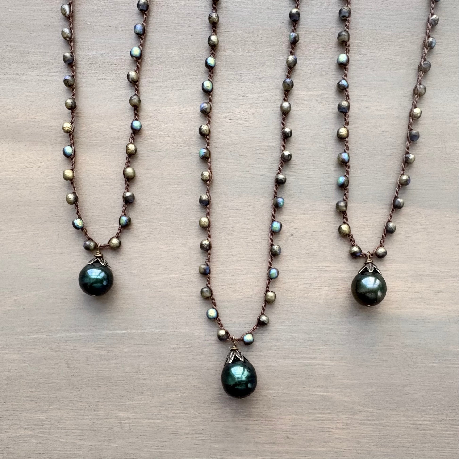 Three pearl necklaces with green teardrop pendants on a beige surface