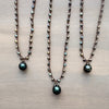 Three pearl necklaces with green teardrop pendants on a beige surface