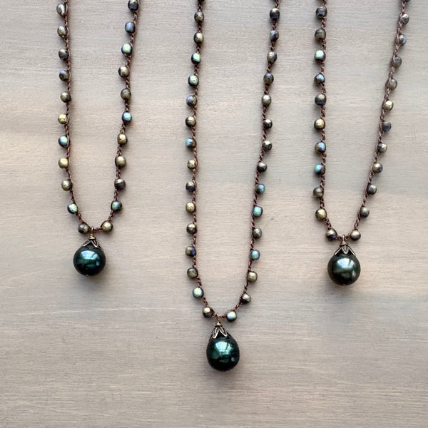 Three pearl necklaces with green teardrop pendants on a beige surface