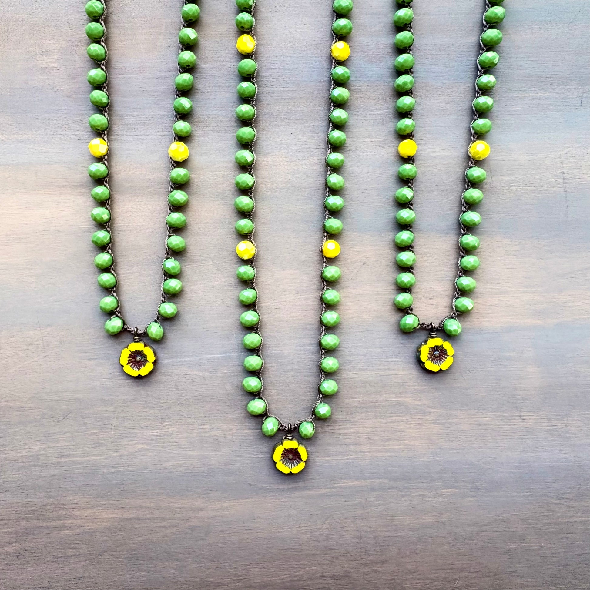 Three green beaded necklaces with yellow flower pendants on a wooden surface
